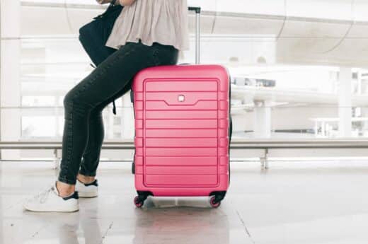 Long flight in economy photo. Picture of a lady sitting on a pink carry on suitcase.