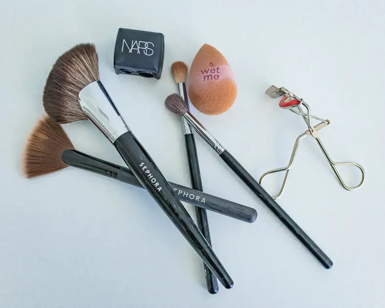 tools to pack like highlighter brush, beauty blender, eyelash curler travel makeup essentials for your trip
