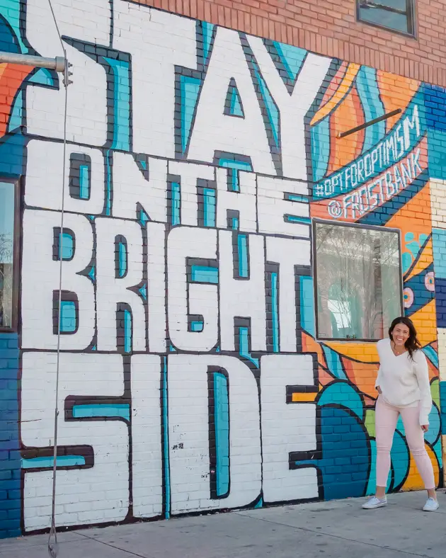 Me posing in front of a wall mural in Deep Ellum that says "stay on on the bright side." 