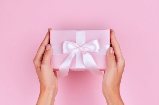 Gift for travel lovers photo os a woman holding a gift with pink wrapping paper and a white bow.